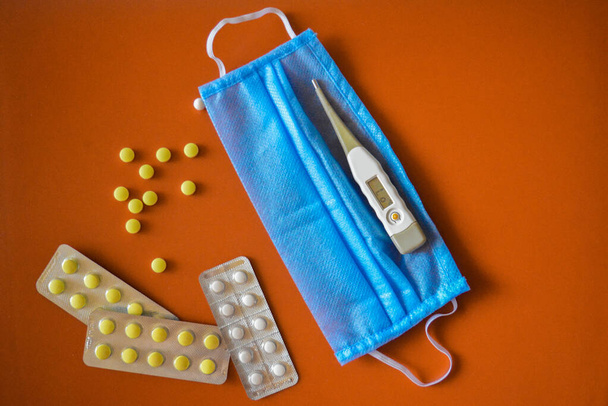 Szétszórt tabletta, orvosi maszk hőmérővel fekszik narancssárga alapon - Fotó, kép