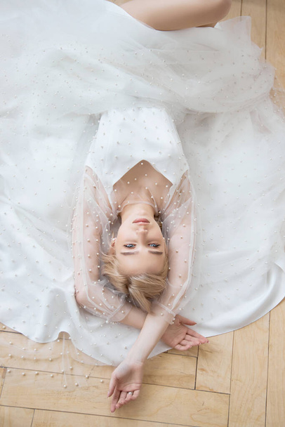 Romantic portrait of a woman on the floor in a beautiful long white dress. The girl is blonde with blue eyes and beautiful makeup on her face. Natural cosmetics - Photo, image