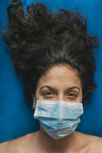 branco caucasiano morena menina com azul médico máscara facial, olhando para a câmera. fundo azul, sem roupas. formato vertical
 - Foto, Imagem