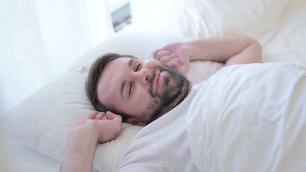 attraktiver Bart junger Mann wacht auf und steigt aus dem Bett  - Foto, Bild
