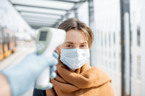 Mesurer la température d'une jeune femme en masque facial à un checkpoint à l'extérieur
 - Photo, image