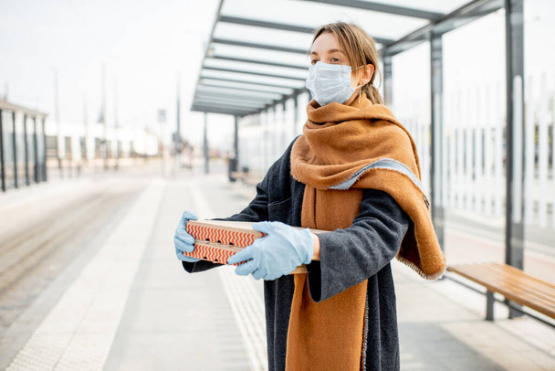 Женщина в медицинской маске и перчатках с едой на вынос на открытом воздухе
 - Фото, изображение