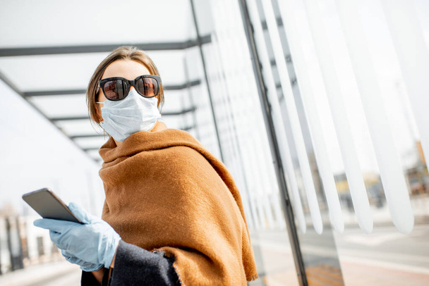 Woman in face mask and gloves with a smart phone during an epidemic outdoors - Fotoğraf, Görsel
