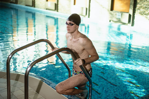 Portrait of a male coach in a cap and swimming goggles. Out of the pool. Posing over water - Zdjęcie, obraz