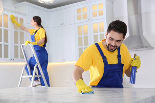 Professional young janitor cleaning table in kitchen - Foto, imagen