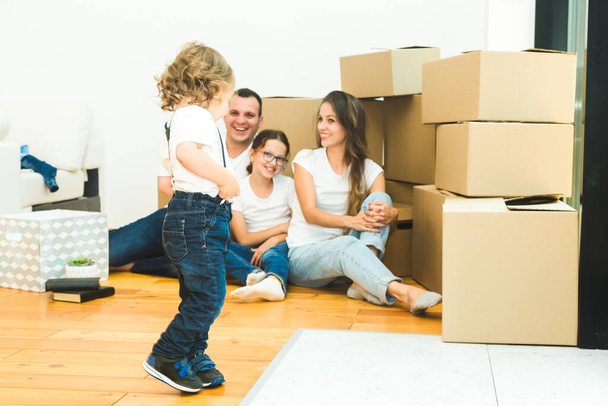 Feliz familia joven, padres hija e hijo, desempacando cajas y mudarse a un nuevo hogar. niños divertidos corren con cajas
 - Foto, imagen