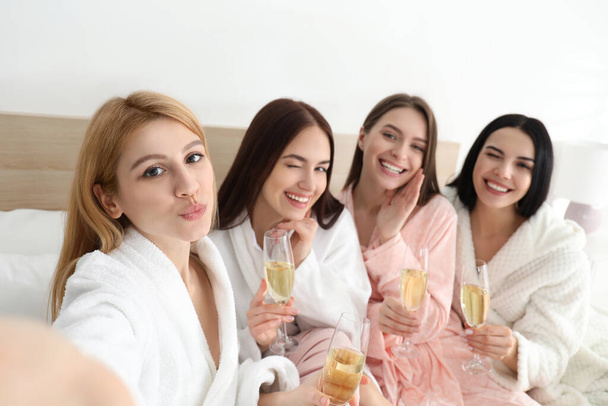 Beautiful young ladies with champagne taking selfie on bed at pamper party. Women's Day - Foto, afbeelding