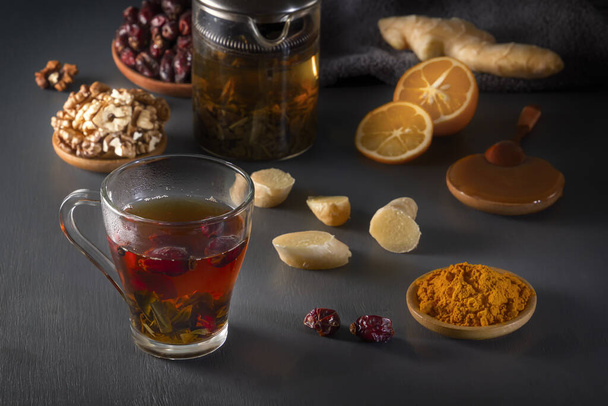 Medicinal herbal tea in a glass cup, ginger, walnut, turmeric, honey, lemon and dry rosehip berries - a means to increase immunity from the virus - Photo, Image