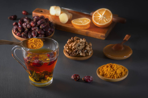 Medicinal herbal tea in a glass cup, ginger, walnut, turmeric, honey, lemon and dry rosehip berries - a means to increase immunity from the virus - Фото, зображення