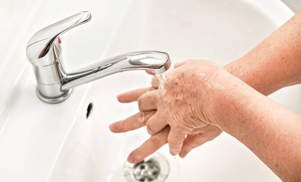 Senior woman washing her hands with soap under tap water faucet. Can be used as hygiene illustration concept during ncov coronavirus / covid 19 outbreak - Fotó, kép