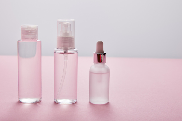 Set of cosmetic bottle, spray and serum on pink and grey background - Фото, зображення