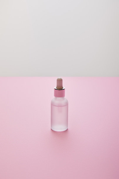 Pembe ve gri zemin üzerinde sıvı bulunan serum şişesinin yüksek açılı görüntüsü - Fotoğraf, Görsel