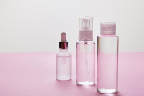Spray, cosmetic bottle and serum bottle with liquid on pink and grey background   - Foto, imagen