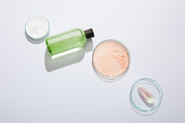 Colocación plana con cristalería de laboratorio, botella cosmética con líquido verde, tarro de crema cosmética y pétalo de rosa sobre fondo gris
 - Foto, Imagen