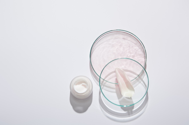 Vista superior de cristalería de laboratorio y tarro de crema cosmética con pétalo líquido y rosa sobre fondo gris
 - Foto, Imagen