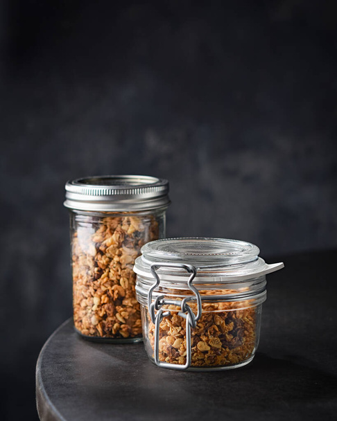 homemade granola, almonds, hazelnuts, raisins, dried cranberries, pumpkin, flax, and sunflower seeds in glass jars. Space for text. Selective focus. Dark background. Healthy superfood concept. - Photo, Image