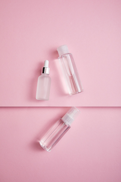Vista dall'alto di bottiglia cosmetica trasparente, spray e bottiglia di siero con liquido su sfondo di carta rosa
 - Foto, immagini