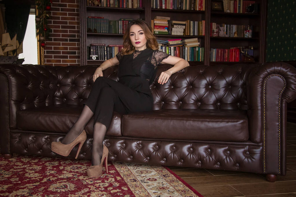 A beautiful stylish woman is sitting on the Chesterfield sofa. Psychologist, wait for your reception, personal secretary, realtor. - Zdjęcie, obraz