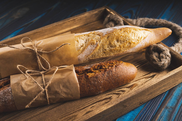 Dos baguettes de trigo y harina de centeno en una bandeja sobre un fondo de madera azul
. - Foto, imagen