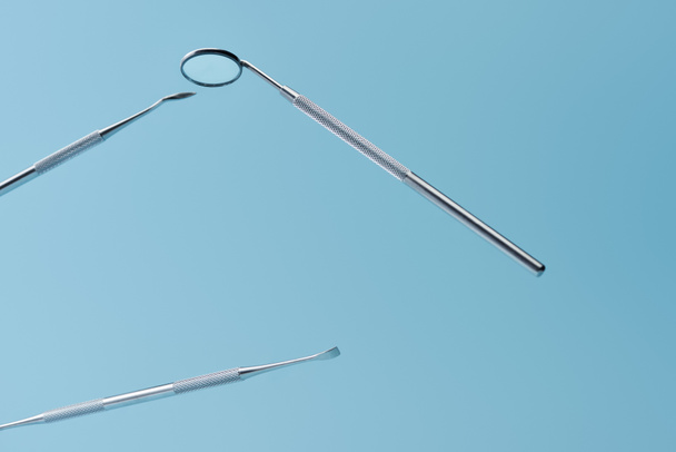 Metal dental instruments levitating isolated on blue background - Foto, afbeelding