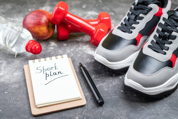Sport shoes, dumbbells, apple and bottle of water on grey background. Concept healthy lifestyle, sport plan, active, sport and diet. Sport equipment. Copy space - Photo, Image
