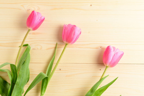 Vue de dessus de trois petites fleurs rose vif de tulipe et feuilles vertes sur une table en bois brut, beau fond floral intérieur photographié avec un petit focus
 - Photo, image