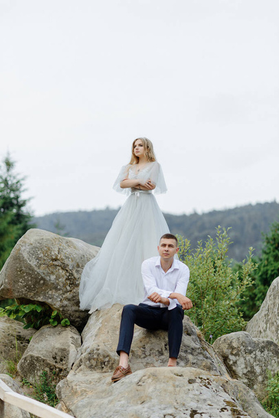 Photoshoot of a couple in love in the mountains. The girl is dressed like a bride in a wedding dress. - Foto, imagen