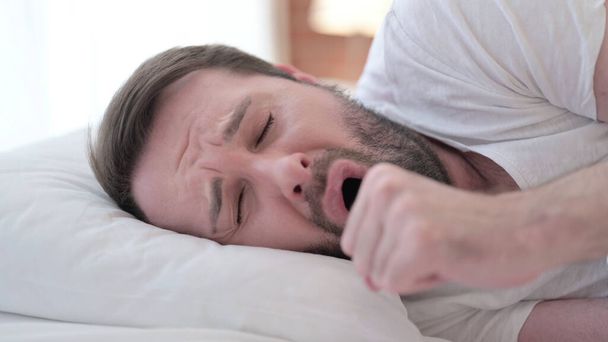 Primer plano de atractivo enfermo barba joven toser en la cama
  - Foto, Imagen