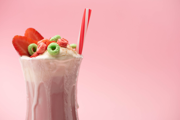 Glass of milkshake with ice cream, colorful candies, strawberry halves and drinking tube on pink background - Photo, Image