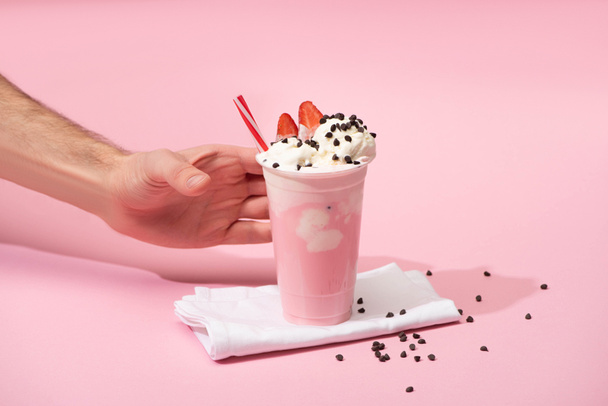 Widok upraw męskiej dłoni z jednorazowym kubkiem koktajlu mlecznego z czekoladowymi kąskami i truskawkami na serwetkach na różowo - Zdjęcie, obraz
