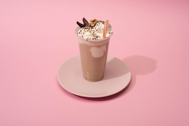 Vista de ángulo alto de la taza desechable de batido de chocolate con paja para beber en el plato sobre fondo rosa
 - Foto, imagen