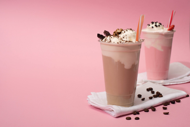 Foco seletivo de copos descartáveis de chocolate e batidos de morango com grãos de café em guardanapos em fundo rosa
 - Foto, Imagem