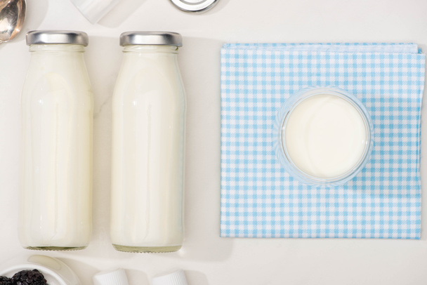 Top view of bottles and glass of homemade yogurt on plaid cloth on white background - Foto, Imagen