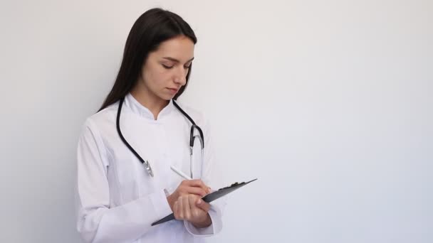 Amistosa doctora, escribe el diagnóstico a la tarjeta de clientes, un estetoscopio en su cuello
 - Imágenes, Vídeo