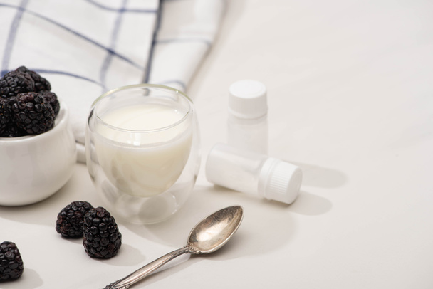 Enfoque selectivo de vaso de yogur, cucharadita, recipientes con cultivos de iniciación y azucarero con moras sobre blanco
 - Foto, imagen
