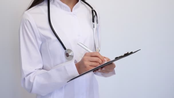 Nahaufnahme freundliche Ärztin, schreibt die Diagnose auf die Kundenkarte, ein Stethoskop am Hals - Filmmaterial, Video