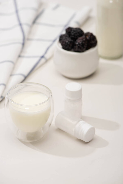 Selektiver Fokus von Glas Joghurt und Behältern mit Starterkulturen in der Nähe von Stoff und Zuckerdose mit Brombeeren auf Weiß   - Foto, Bild