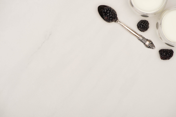 Top view of glasses of homemade yogurt and teaspoon with blackberries on white background - Zdjęcie, obraz