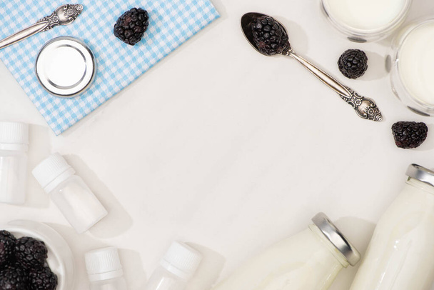 Vista dall'alto di bottiglie e bicchieri di yogurt fatto in casa, cucchiaini, bacche e contenitori con colture di antipasto su bianco
  - Foto, immagini