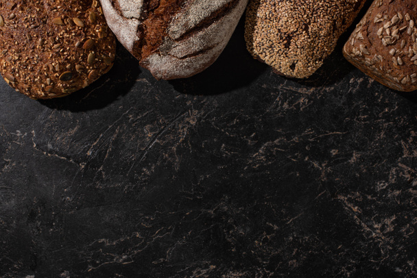 bovenaanzicht van vers gebakken volkoren brood op stenen zwarte ondergrond - Foto, afbeelding