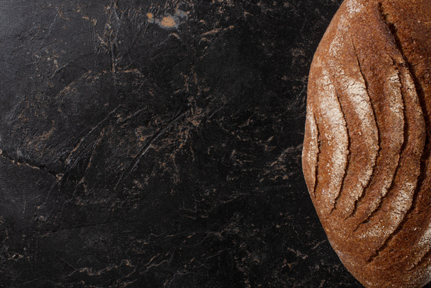 top view of fresh baked brown bread loaf on stone black surface - Fotó, kép