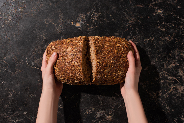 Kırpılmış kadın elinde kepekli tahıllı ekmeği taştan siyah bir yüzeyde tutuyor. - Fotoğraf, Görsel