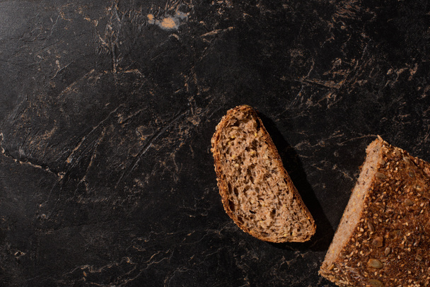 top view of cut whole grain bread on stone black surface - Fotoğraf, Görsel