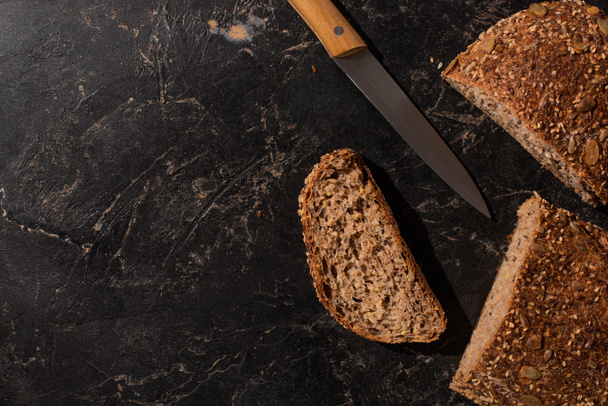 вид сверху на разрезанный хлеб из цельного зерна и нож на каменной черной поверхности
 - Фото, изображение