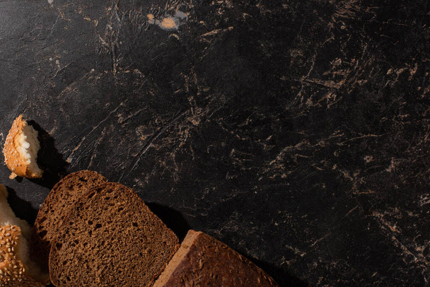 top view of cut brown bread on stone black surface - Zdjęcie, obraz