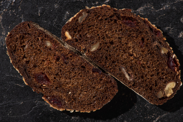 top view of fresh baked black bread slices with nuts on stone black surface - Photo, Image