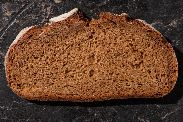 top view of brown bread slice on stone black surface - Foto, Imagem