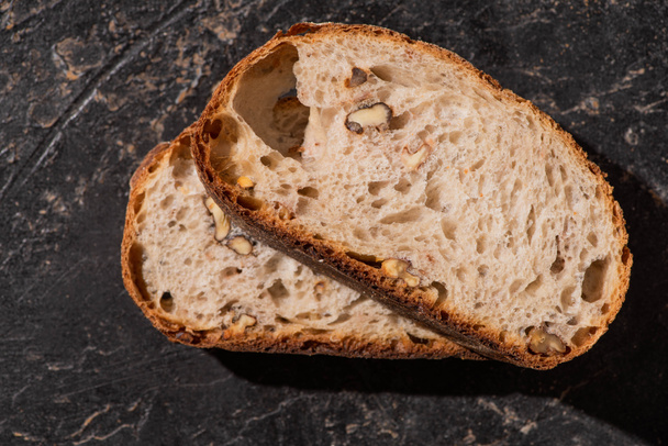 Taze tahıllı ekmeğin üst görüntüsü. Taştan siyah yüzeyde fındıklı dilimler. - Fotoğraf, Görsel