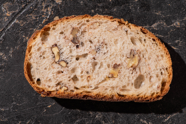 top view of fresh whole grain bread slice with nuts on stone black surface - Fotó, kép
