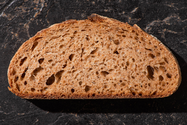 top view of brown bread slice on stone black surface - Fotó, kép